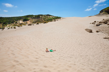 Fototapeta na wymiar little girl lying on sand under the dune in horizon