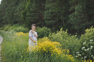 Fototapeta premium A beautiful girl in a long light dress in a clearing with yellow flowers 1705