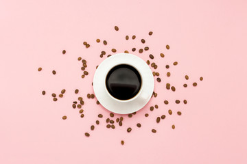 White cup with black coffee, grains of coffee, on a pink background. Flat lay, top view