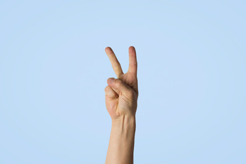 Male hand with two fingers raised against a blue background. Side picture. Peace gesture, greeting