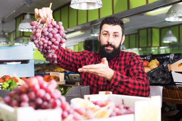 Adult male seller offering grapes in shop