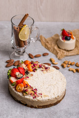 White cake with berries on the table with nuts, cinnamon, a glass, lemon.