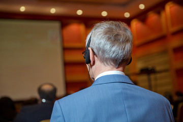 Unrecognizable business people using headphones for translation during event . bald security guard with the headset to control people . heated debate at a conference discussion