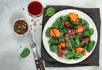 Warm spinach salad with chicken liver and baked pumpkin with spices and balsamic. Delicious dinner with red wine for gourmets.