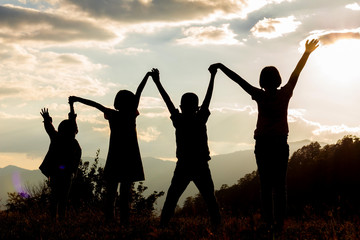 Fototapeta na wymiar Silhouette group children with raised hands on mountain at sunset time.