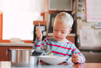A handicapped down syndrome child pouring soup into a plate indoors.