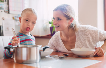 A handicapped down syndrome child with his mother indoors eating lunch.