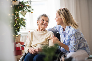 A senior woman in wheelchair with a health visitor at home at Christmas time. - obrazy, fototapety, plakaty