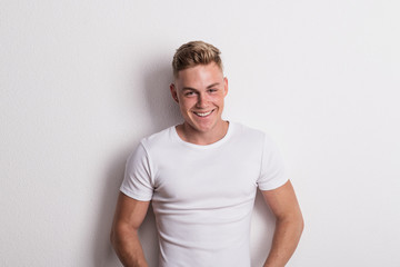 Portrait of a young man in white T-shirt in a studio, leaning against wall. - Powered by Adobe