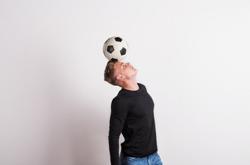 Portrait of a young man with football ball on head in a studio. Copy space.