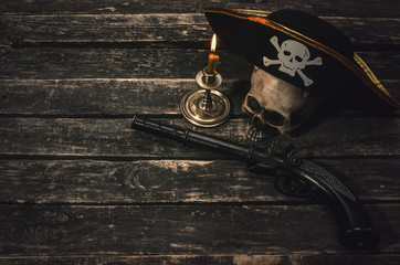 Pirate captain table with pirate hat, human skull, musket and burning candle. Treasure hunter concept background.