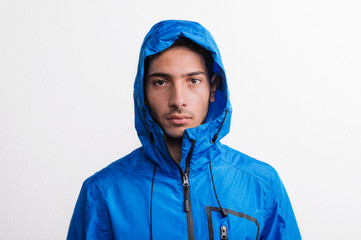 Portrait of a young serious hispanic man with blue anorak in a studio.. © Halfpoint