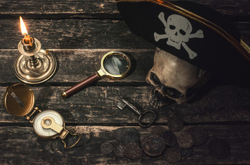 Pirate captain table with pirate hat on the human skull, compass, magnifying glass, mooring rope, coins, key of treasure chest and burning table. In the searching of gold.
