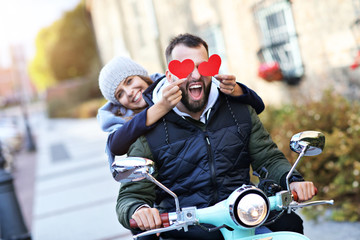 Beautiful young couple holding hearts while riding scooter in city in autumn