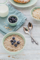 Oatmeal porridge bowl on the white wooden background.