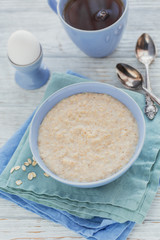 Oatmeal porridge bowl on the white wooden background.