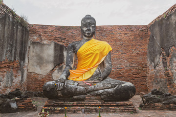 Sitting Buddha sculpture with golden cassock in Wat Wora Chet Tha Ram Temple, Ayutthaya, Thailand among old brick walls, vintage style