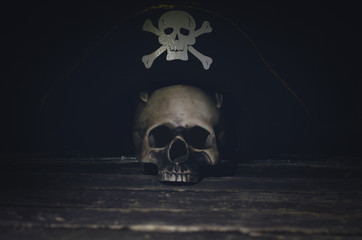 Human skull with pirate captain hat on the wooden table.