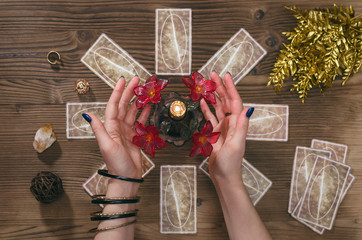 Tarot cards and hands of fortune teller on wooden table background.