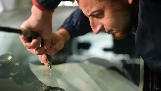 Close-up of a man professionally in the workshop engaged in eliminating cracks on the windshield of the car. Air Drying
