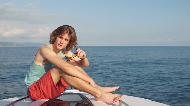 Young caucasian young man on vacation sailing in the sea, sitting on a bow of a motor boat , looking at camera