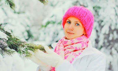 Beautiful girl wearing colorful knitted hat scarf near christmas tree over snowy background