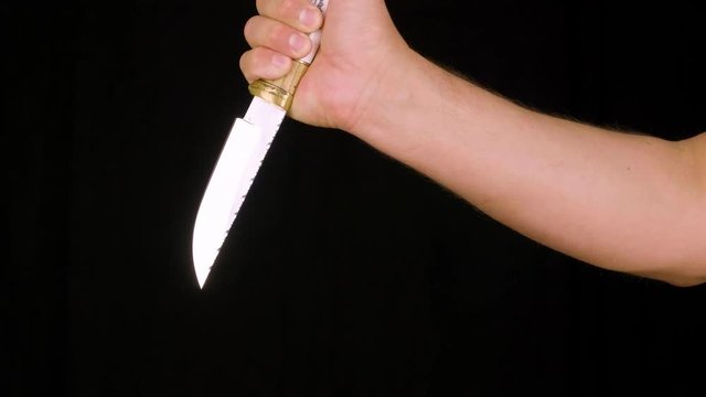 Male hand showing knife with sharp blade and decorative handle, black background