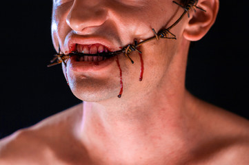 barbed wire, in the mouth, portrait on black background, blood on face