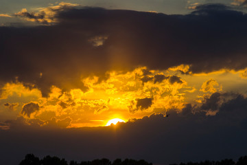 Sunset on a blue sky background - golden rays of the sun, dark clouds and a flying helicopter.