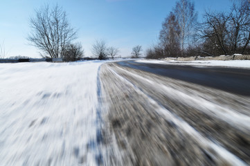 Traces of a car tires on the road  in motion covered in snow against blue sky