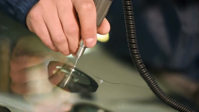 Close-up of a man professionally in the workshop engaged in eliminating cracks on the windshield of the car. Polymer drainage drilling