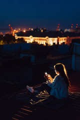 Fototapeta premium Young girl sits at night on the roof of a house. Beautiful evening