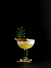 Cold yellow pear cocktail with ice and dried crushed slices. Restaurant serve, on a black background.