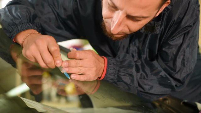 Close-up of a man professionally in the workshop engaged in eliminating cracks on the windshield of the car. Filling the crack with polymer