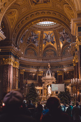 The interior of the main Basilica of Hungary, a large Christmas tree inside the church and many people came to pray at the Christmas. Many gold decorations and icons.