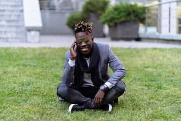 Beautiful business man Afro-American appearance. Sits in the park on a grass wearing spectacles.