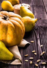 Big yellow pumpkin and pears lie on a beige napkin and pumpkin seeds in a wooden bowl on a black wooden table