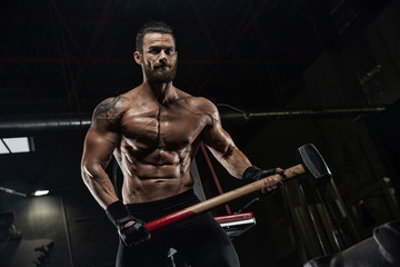 Young handsome athlete bodybuilder, weightlifter, doing crossfit, with a sledgehammer, in a modern gym. Concept-strength, beauty, power, sport, health, sports nutrition, diet, styroydy, scales. - obrazy, fototapety, plakaty