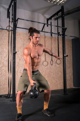 Strong young man lifting weight ball in the gym.