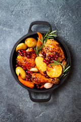 Roasted chicken legs with root vegetables, lemon, garlic, cranberry and rosemary on pan, on black slate stone background