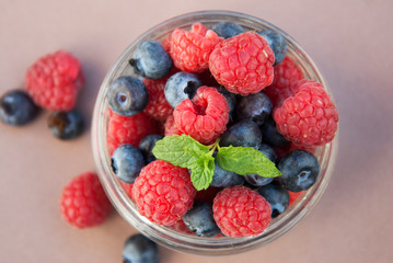 Small glass bowl full of blueberries and raspberries, ready to eat, placed on rustic wood desk.