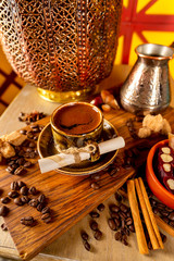 Cup of turkish black coffee on a plate at a wooden board at decorated table with candles, beans and sweets background.