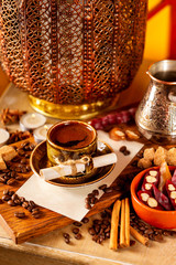Cup of turkish black coffee in a plate with blank paper sheet on a wooden board at decorated table with candles, beans and sweets background.
