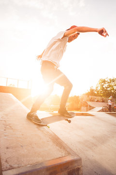 Male teenager performing skateboard tricks against golden sunset