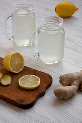 Glass jars of homemade ginger tea with lemon over white wooden background, side view.