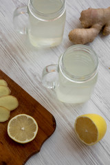Glass jars of homemade ginger tea with lemon over white wooden background, low angle view.