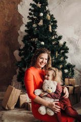 little girl and mother sitting near Christmas tree in cozy room