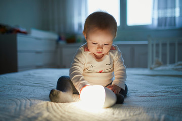 Adorable baby girl playing with bedside lamp in nursery