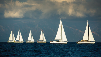 Fototapeta premium Sailing boats participate in yachting regatta among Greek islands in the Aegean Sea in stormy weather.