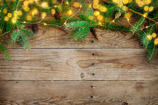 Christmas background with fir tree branches and lights on wooden board